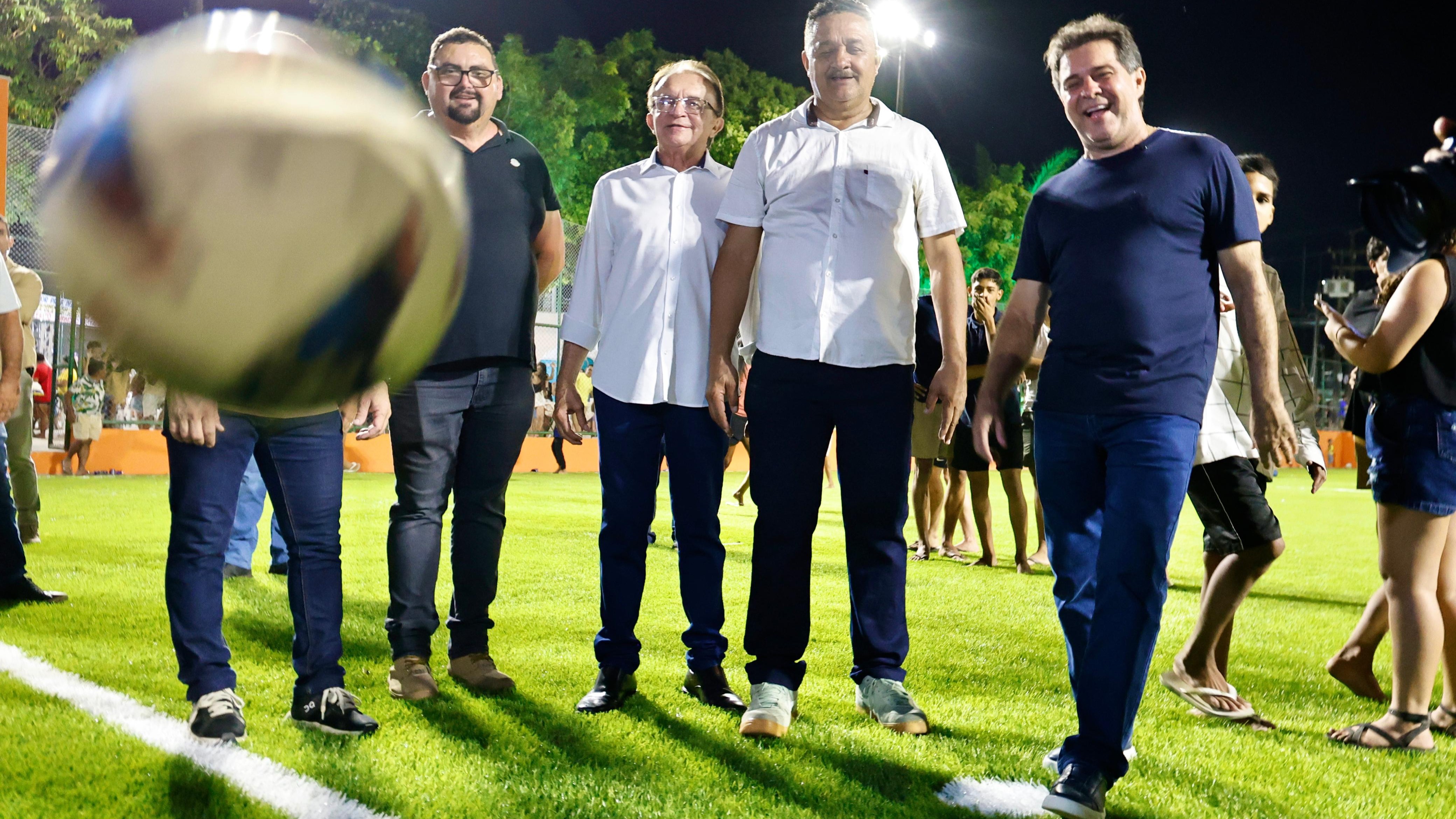 O prefeito Evandro Leitão e apoiadores posam para foto na areninha da praça recém inaugurada. Uma bola aparece no ar em primeiro plano